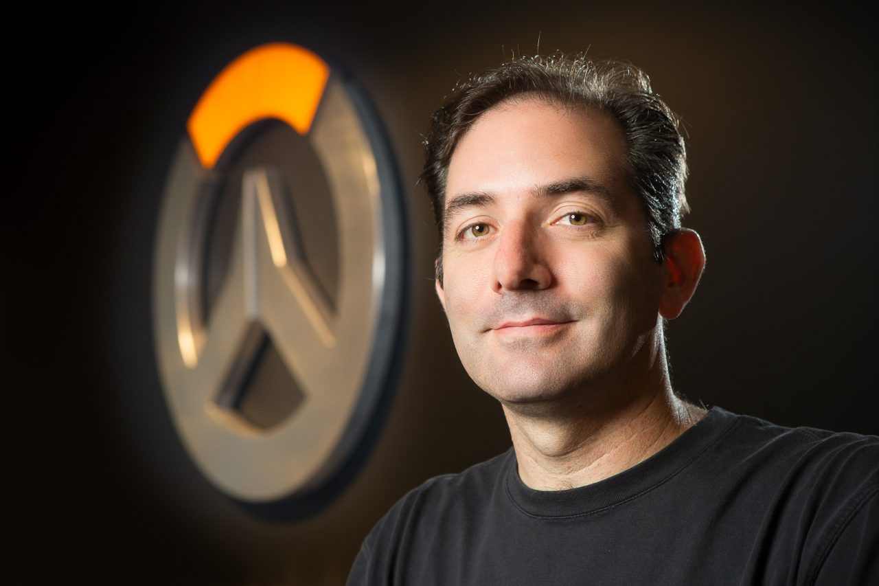 Headshot of a Blizzard Entertainment staff member standing before the Overwatch logo.