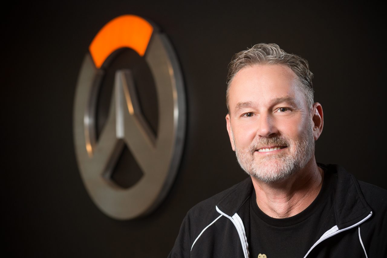 Headshot of a Blizzard Entertainment staff member with the Overwatch logo blurred in the background.