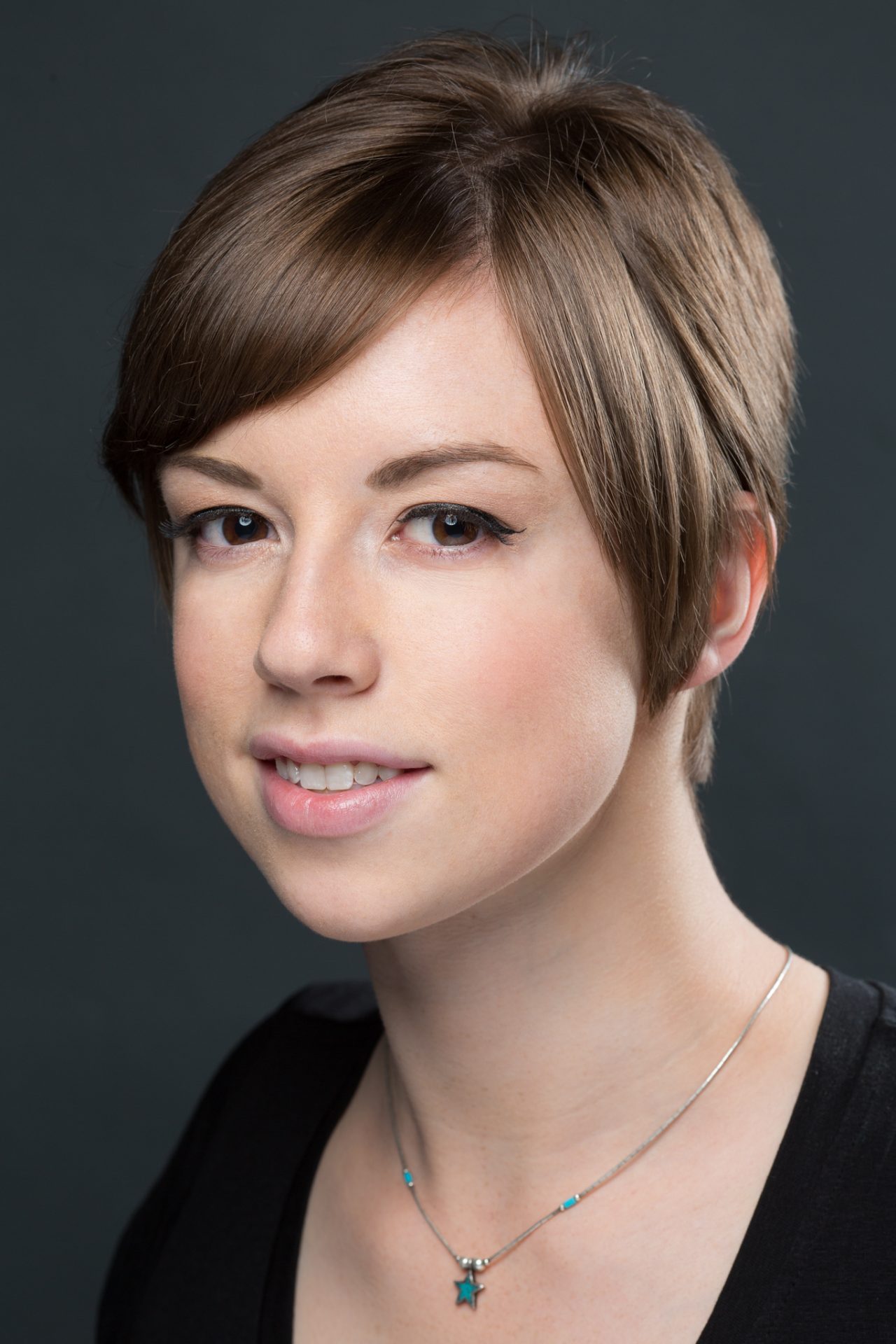 A person with short hair smiles softly in a clean studio headshot, wearing a star necklace.