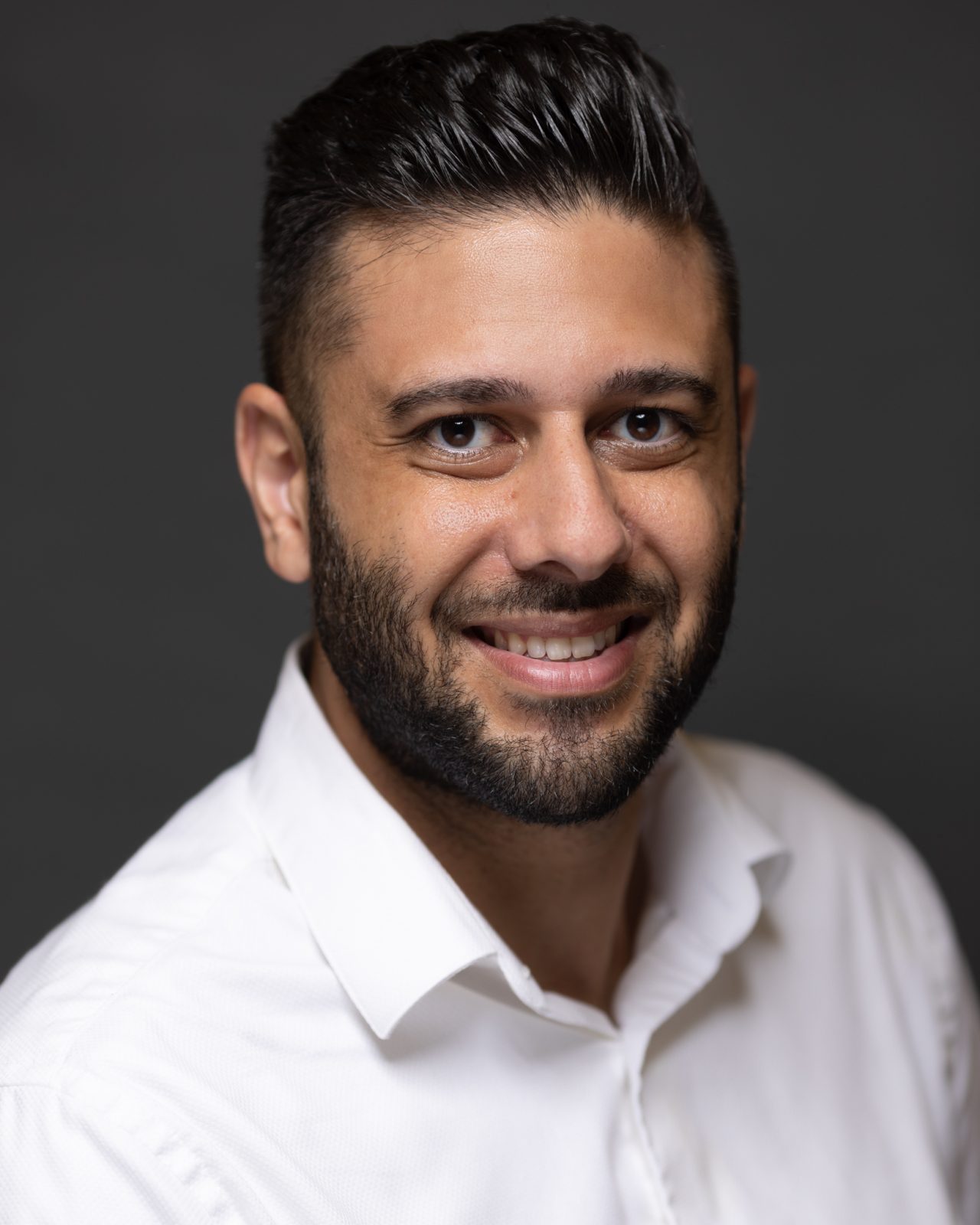 A person in a white collared shirt smiles in a studio-style corporate headshot.
