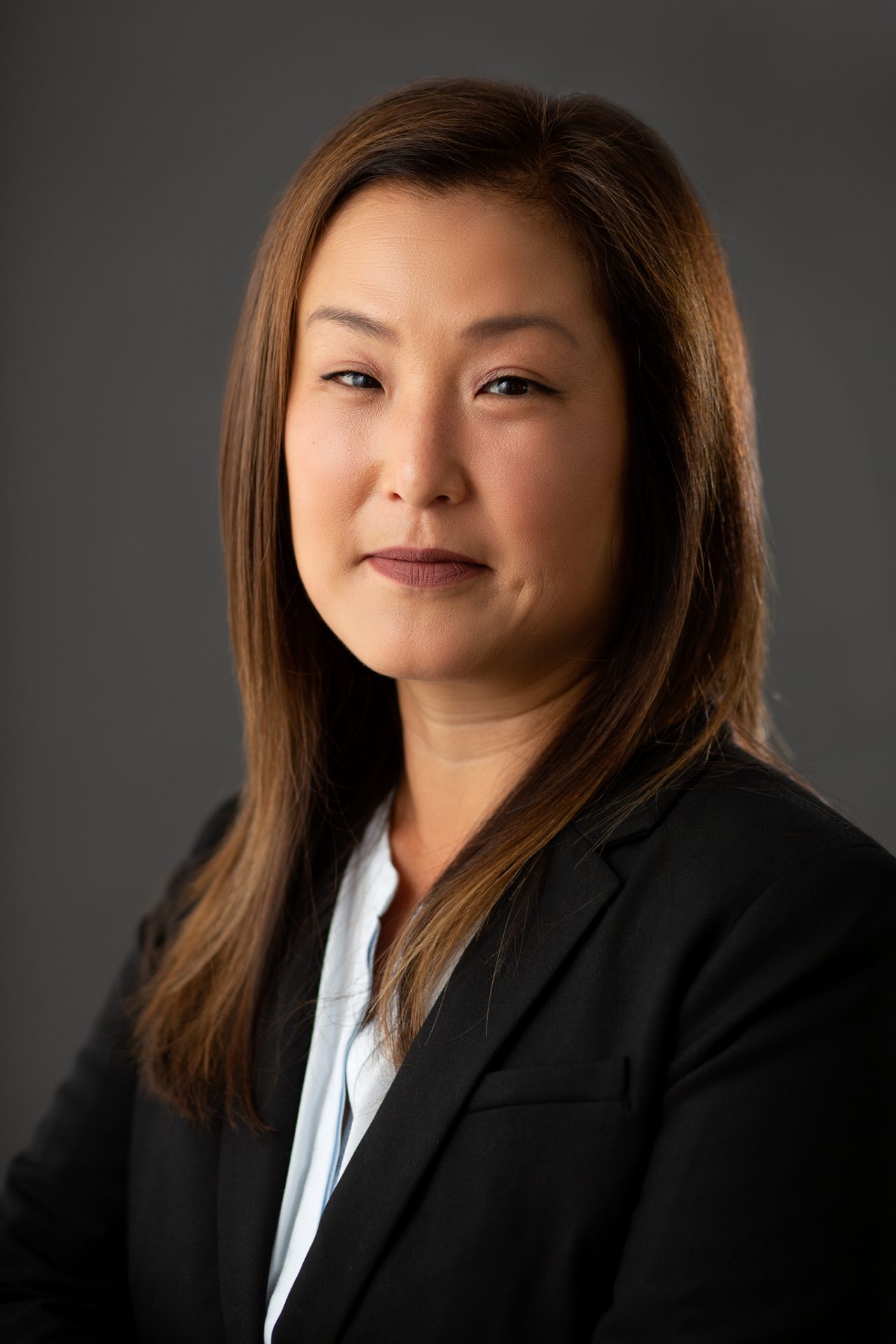 A real estate agent in a blazer poses in a studio setting with soft, even lighting.