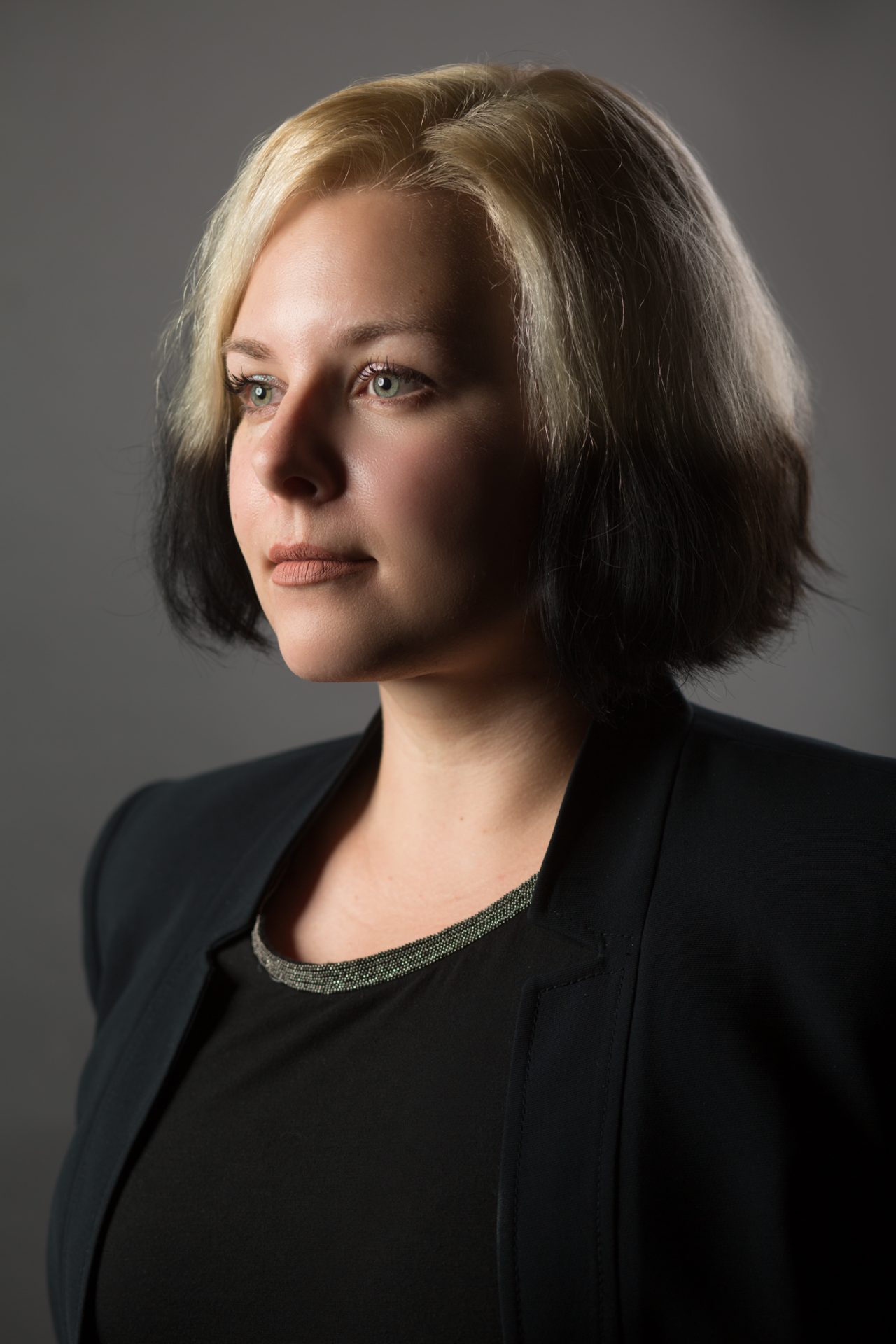 A person with short two-tone hair looks confidently into the distance in a dramatic studio headshot.