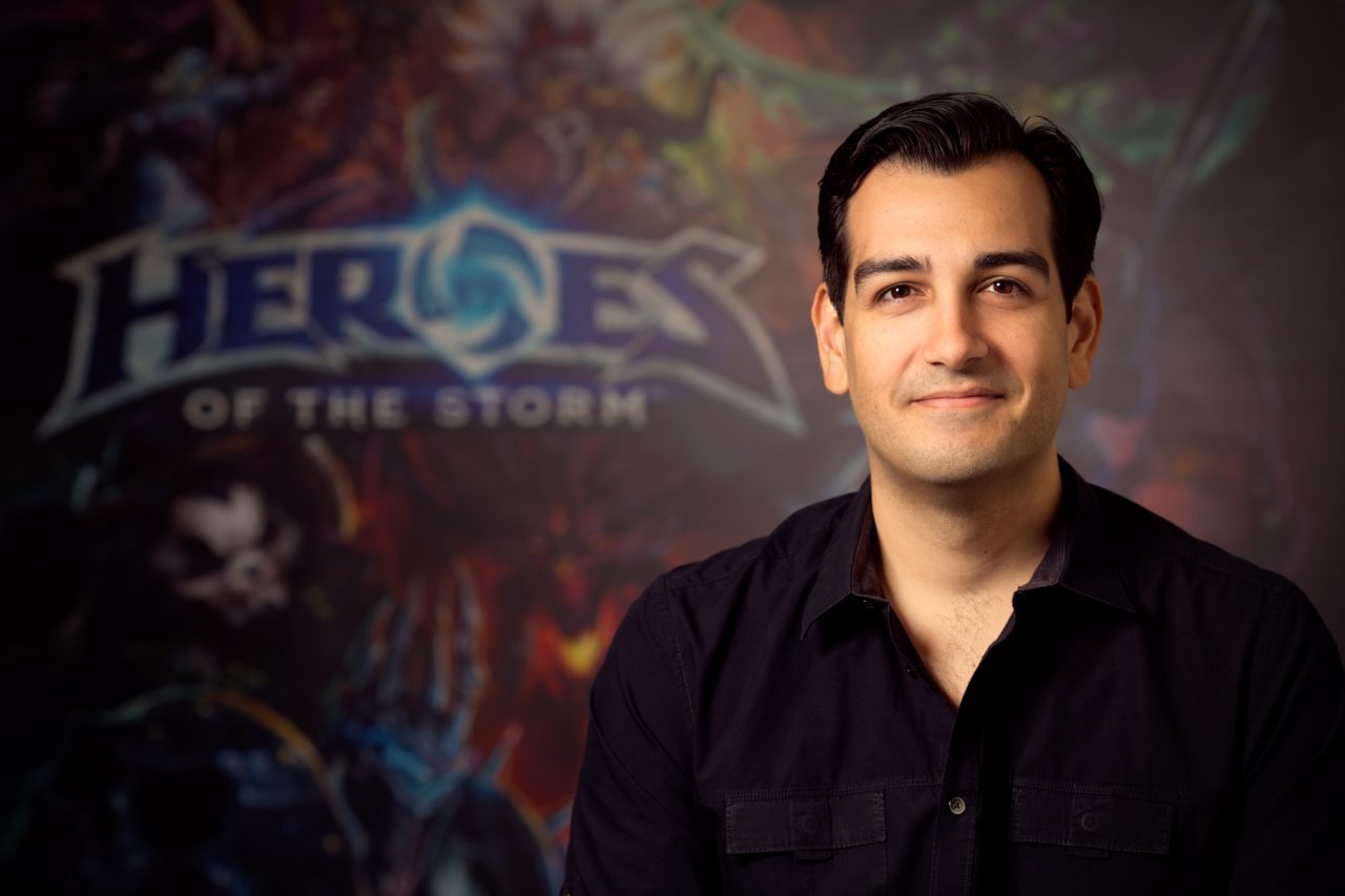 Professional headshot of a person standing in front of a blurred Heroes of the Storm promotional backdrop.